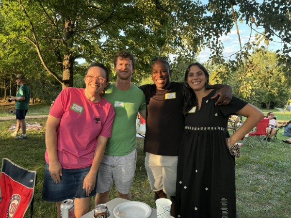 Four neighbors standing together on the grass in the evening light, name tags on