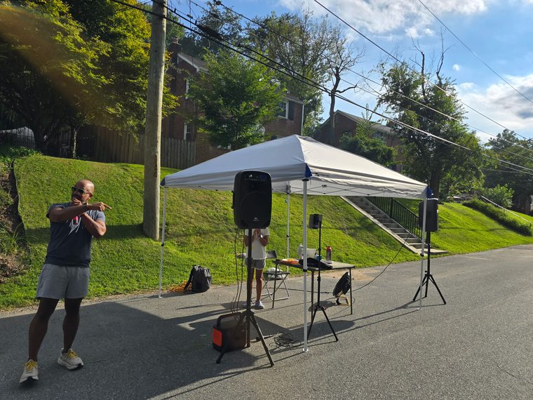 A canopy, two PA speakers on stands and a folding table set up in the middle of an empty street